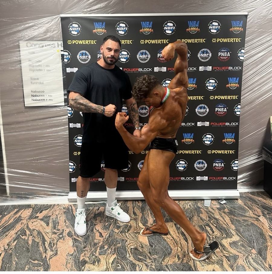 Riccardo Matterazzo accanto al suo atleta in posa con la medaglia al collo, davanti al fondale NBFI / INBA Global